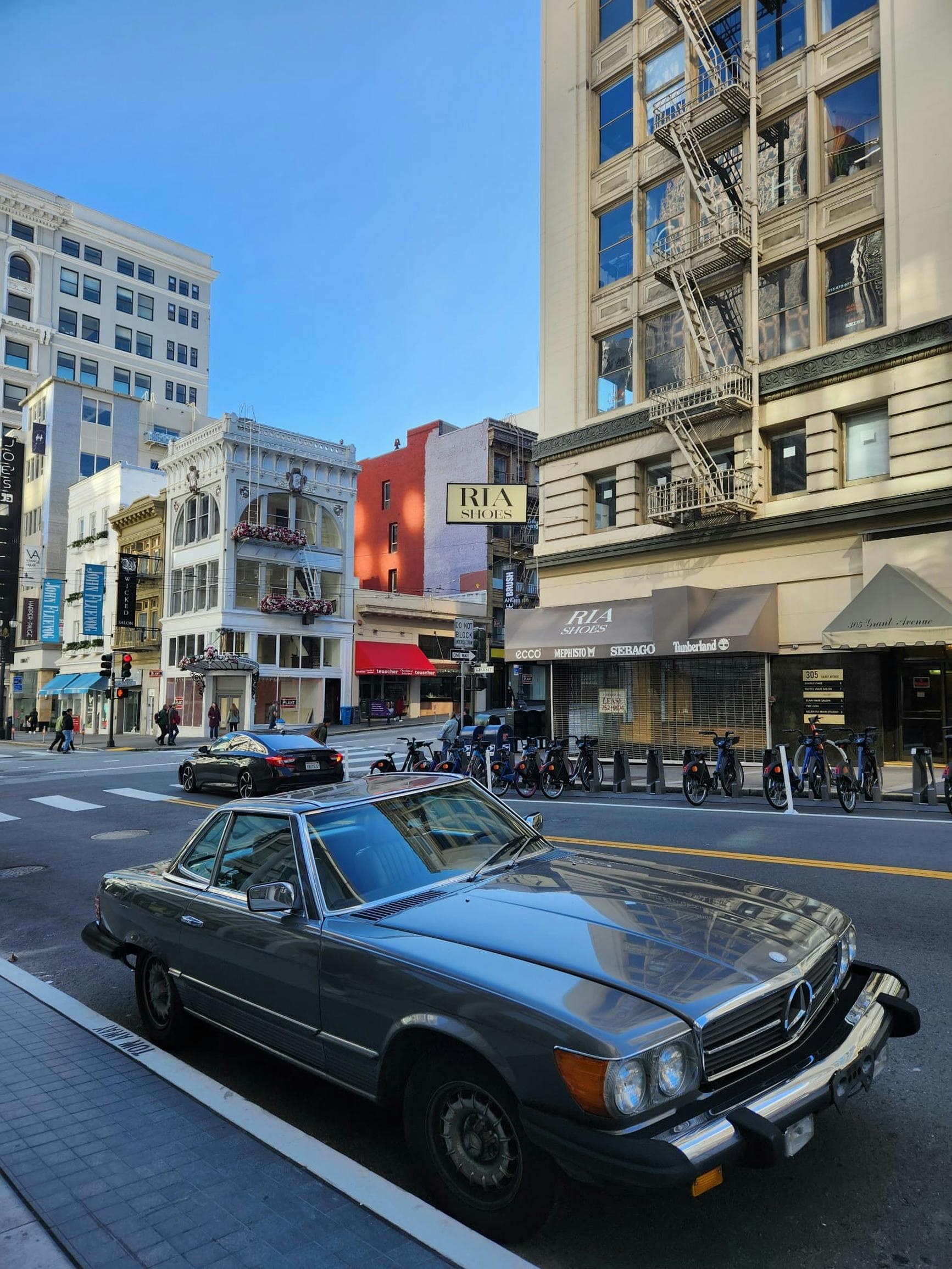 A classic vintage car parked on a lively street corner in San Francisco, CA with urban buildings.