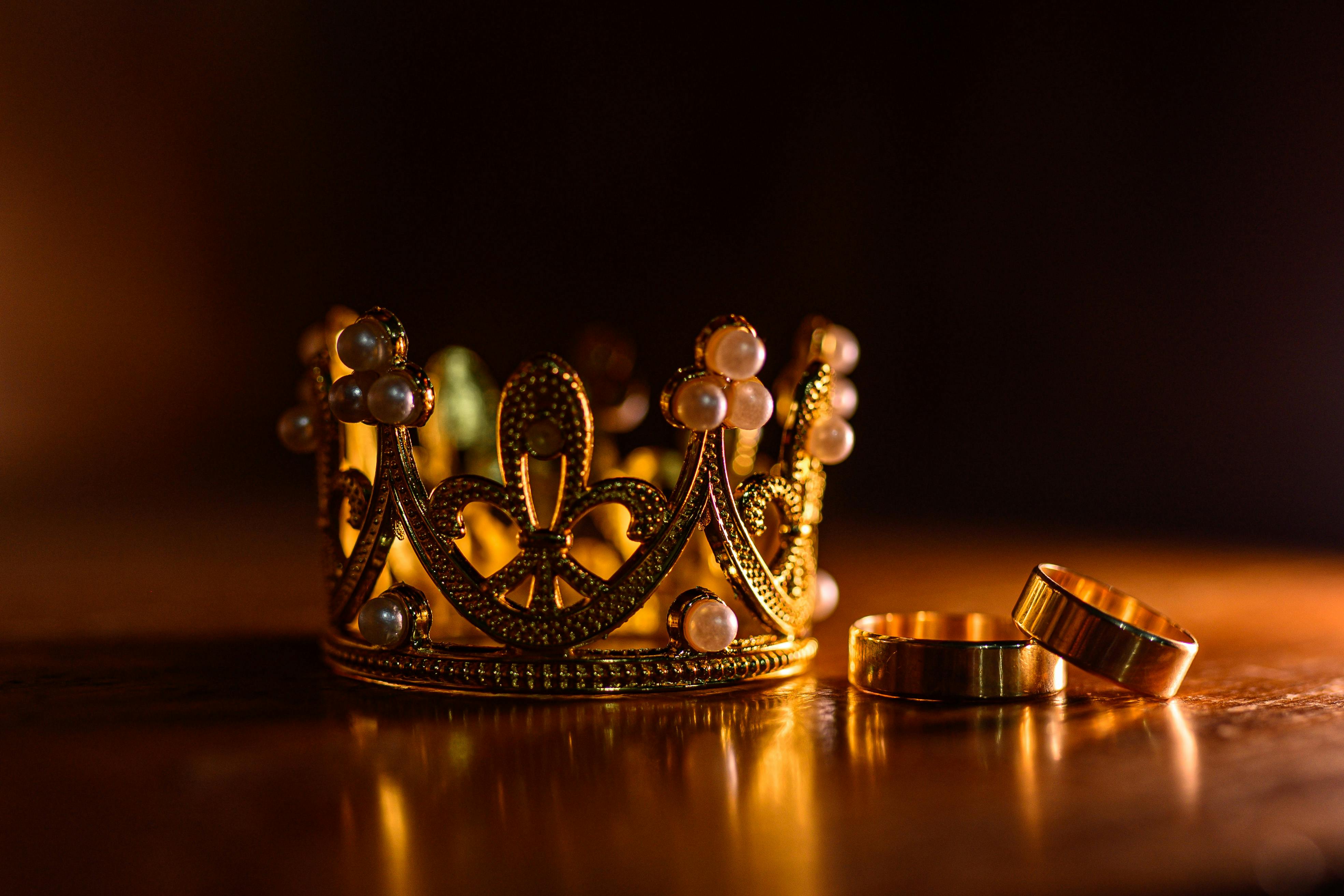 Close-up of an elegant gold crown adorned with pearls and rings on a wooden surface.